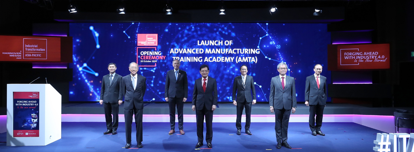 Seven people stand on stage at the "LAUNCH OF ADVANCED MANUFACTURING TRAINING ACADEMY (AMTA)".